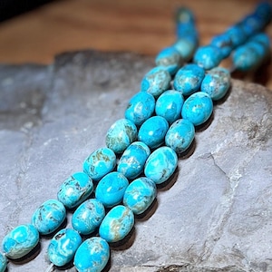 May include: Strands of turquoise gemstone beads. The beads are oval-shaped with a polished finish, displaying a vibrant turquoise color with brown and gray veining. The beads are strung together, creating a necklace or bracelet.