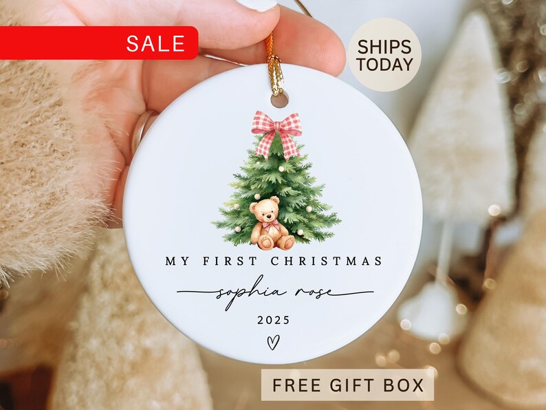 May include: White ceramic Christmas ornament with a watercolor illustration of a Christmas tree, teddy bear, and a red and white plaid bow. Text reads "My First Christmas" and "Sophia Rose 2025". Includes a gold string for hanging.