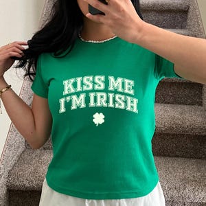 May include: Green short-sleeved t-shirt with white text that reads "Kiss Me I'm Irish" and a white shamrock.