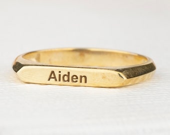 May include: A gold band ring with a rectangular shape and the name "Aiden" engraved on the top.