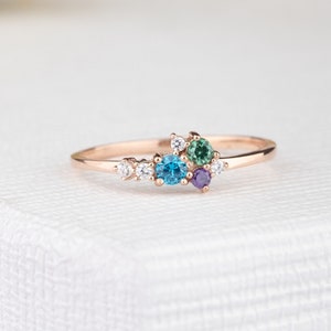 Könnte beinhalten: Ein zarter Ring aus Roségold mit einem Cluster aus bunten Edelsteinen. Der Ring verfügt über einen blauen Topas, einen grünen Peridot, einen violetten Amethyst und mehrere kleine weiße Diamanten.