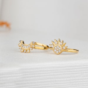 May include: Two gold rings with clear cubic zirconia stones. One ring is a crescent moon shape and the other is a sun with a starburst design.