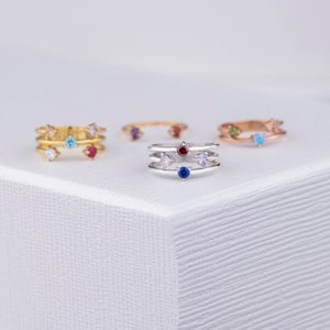 May include: Four silver rings with colorful gemstones. The rings are stacked on top of each other and have a delicate design. The gemstones are blue, red, pink, and purple.