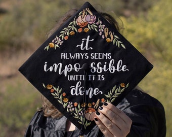 May include: Black graduation cap with embroidered floral details and the text "it always seems impossible until it is done."