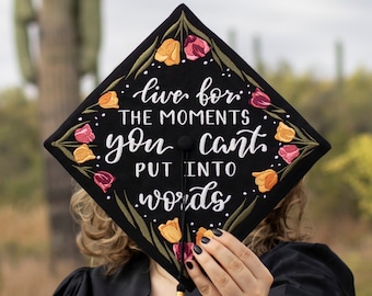 May include: Black graduation cap with embroidered flowers and the quote "live for the moments you can't put into words".