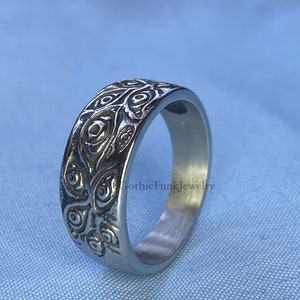May include: A silver-toned ring with an intricate, embossed floral pattern. The ring's band is wide, and the design wraps around the entire circumference. The text "GothicFunkJewelry" is visible on the side of the ring.