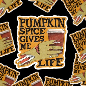 May include: A sticker with a zombie hand holding a cup of pumpkin spice coffee. The sticker says "Pumpkin Spice Gives Me Life".