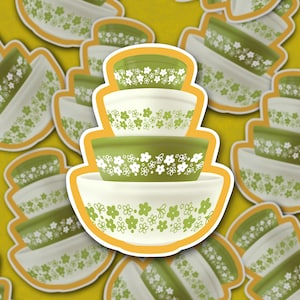 May include: A set of three green and white mixing bowls with a floral pattern. The bowls are stacked on top of each other and have a yellow outline.