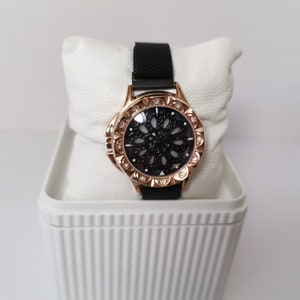 May include: A black and rose gold watch with a black face and a mesh band. The watch face has a decorative design with rhinestones around the edge.