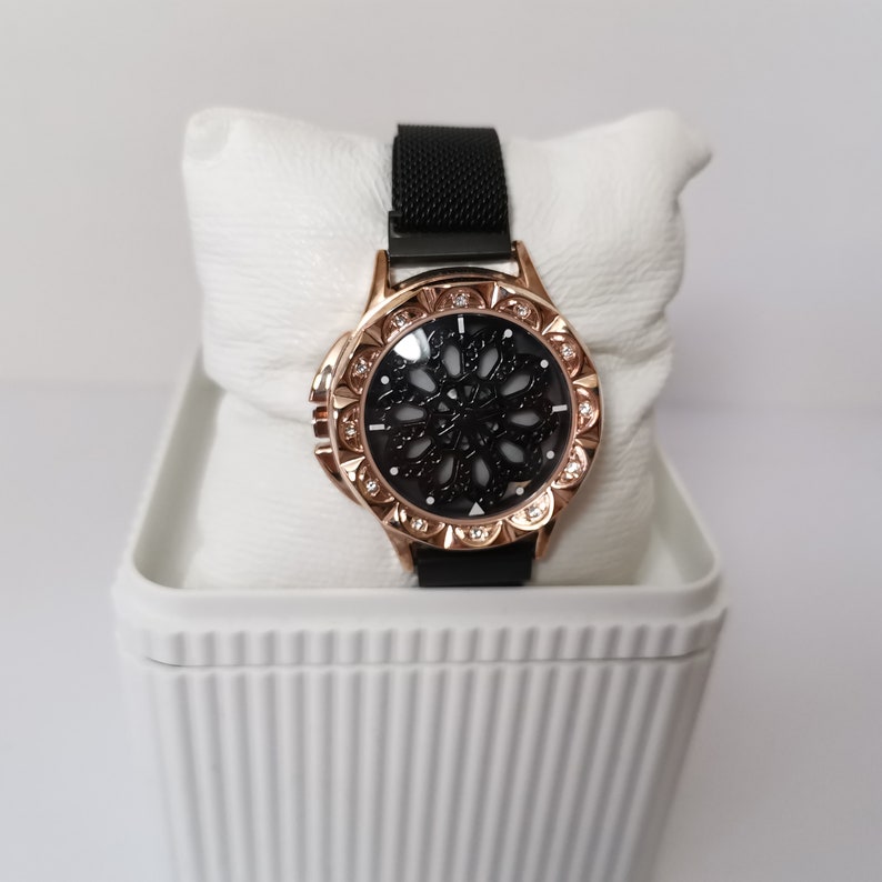 May include: A black and rose gold watch with a black face and a mesh band. The watch face has a decorative design with rhinestones around the edge.