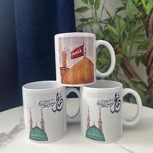 Può includere: Tre tazze di ceramica bianca impilate. La tazza superiore presenta un'illustrazione di una moschea con una bandiera rossa e testo arabo. Le altre due tazze hanno un'illustrazione di una moschea a cupola verde e calligrafia araba.