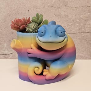 May include: A whimsical, rainbow-colored chameleon planter embracing a tree stump-shaped pot filled with succulents. The chameleon's body transitions from blue to yellow to pink and purple. The planter is a unique decorative item.