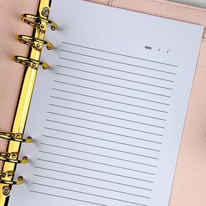 Pu&ograve; includere: Una pagina bianca con carta rigata in un'agenda rilegata in pelle rosa con anelli dorati. La pagina ha la parola "data" scritta in alto con uno spazio per la data.