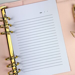 Pu&ograve; includere: Un'agenda rilegata in pelle rosa con anelli dorati e una pagina bianca con righe aperta su una pagina bianca con la parola "data" scritta in alto.