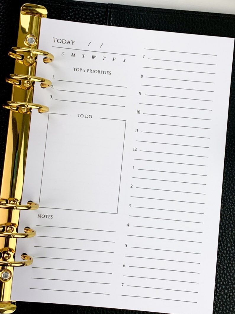 May include: A white daily planner with a gold binder. The planner has sections for "Today", "Top 3 Priorities", "To Do", and "Notes".
