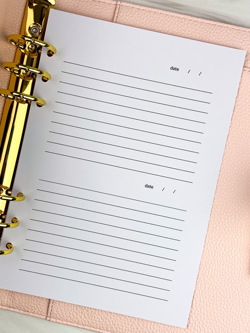 May include: A white planner with gold rings and lined pages. The planner has two sections with the word "date" and a space for writing the date.