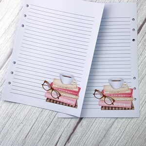 May include: Two white lined pages with holes on the left side. Each page has a stack of pink and brown books with a coffee cup on top and a pair of glasses next to the books. The books have the text "BURBERRY" and "GABBANA" on them.
