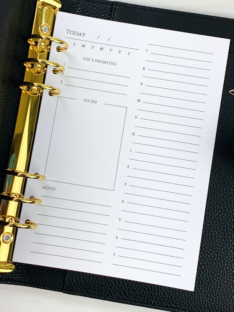 May include: A white daily planner page with a gold binder. The page is divided into sections for "Today", "Top 3 Priorities", "To Do", and "Notes".