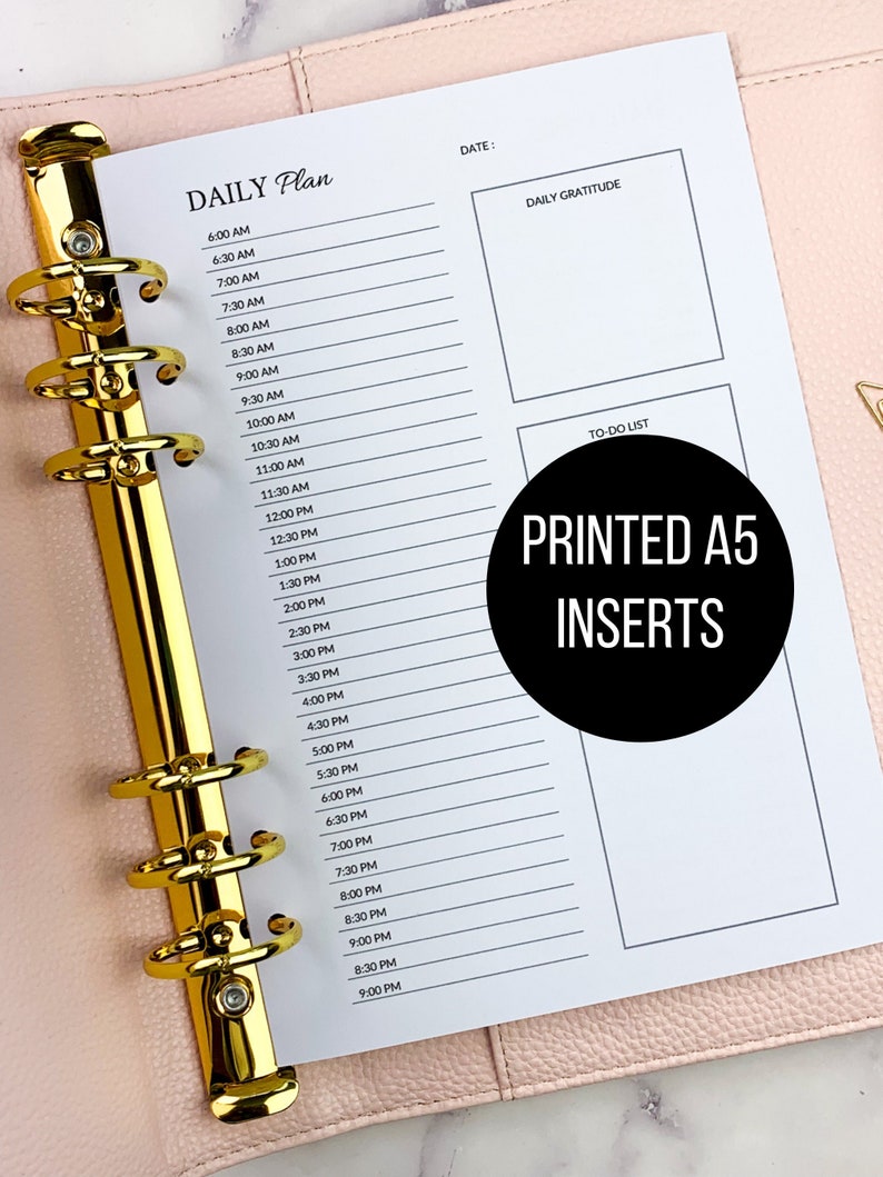 May include: A white A5 planner insert with a daily schedule from 6:00 AM to 9:00 PM, a section for daily gratitude, and a to-do list. The text "PRINTED A5 INSERTS" is printed in black on a white circle.