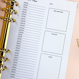 May include: A daily planner with a white background and black text. The planner has sections for daily gratitude, to-do list, and notes. The planner is divided into hourly time slots from 6:00 AM to 9:00 PM.