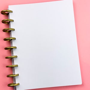 Puede incluir: Un cuaderno blanco de espiral con anillos dorados sobre un fondo rosa.