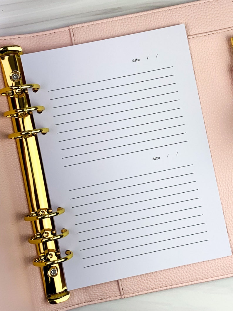 May include: A white page with lined paper and the word "date" written at the top and bottom of the page. The page is in a gold and pink binder.