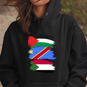 以下が含まれることがあります： 3つの旗が縦に積み重ねられたグラフィックがプリントされた黒いパーカー。旗はパレスチナの国旗、コンゴ民主共和国の国旗、スーダンの国旗です。