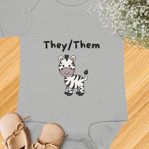 May include: A gray baby onesie with the text "They/Them" and a black and white zebra illustration.