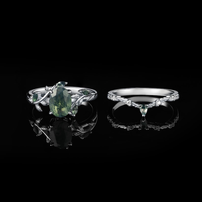 May include: Two silver rings. One ring features a large, oval-cut green gemstone with a leafy vine design. The other ring is a silver band with small clear gemstones and a small green gemstone.