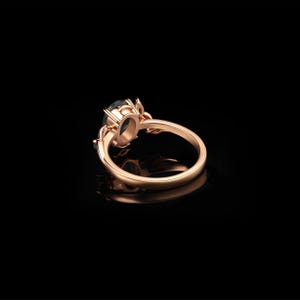 May include: Rose gold ring with a dark teal oval gemstone. The ring features a detailed floral design around the gemstone and on the band. The ring is set against a black background, highlighting its elegant design.