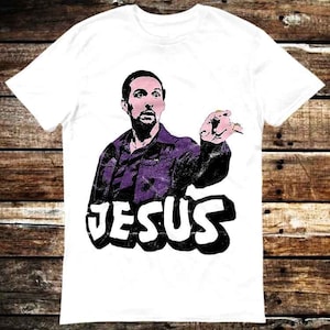 Könnte beinhalten: Weißes T-Shirt mit einem Grafikdruck eines Mannes in einer lila Jacke mit dem Wort "JESUS" in großen schwarzen Buchstaben.