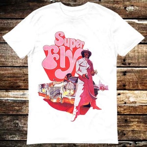 May include: White t-shirt featuring a pink and red graphic of a man in a white suit holding a gun, standing next to a gold car. The graphic also includes the text "Super Fly".