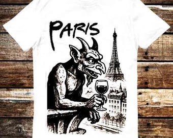 May include: White t-shirt featuring a black and white illustration of a gargoyle holding a wine glass, with the Eiffel Tower and the word "PARIS" in a stylized font. The design is centered on the front of the shirt.