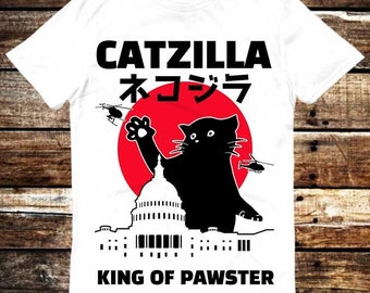 Może przedstawiać: Biała koszulka z nadrukiem czarnego kota w koronie, stojącego na szczycie Kapitolu Stanów Zjednoczonych. Na koszulce widnieje napis "CATZILLA ネコジラ KING OF PAWSTER".