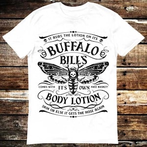 May include: White t-shirt with a black and white graphic design featuring a moth with a skull on its head. The graphic includes the text "It rubs the lotion on its Buffalo Bills, comes with its own free basket! Body Lotion, Skin or else it gets the hose again."
