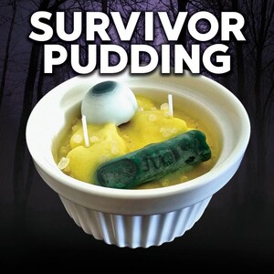 May include: A white ceramic bowl filled with yellow candle wax, a green candle, and a white eyeball candle. The bowl is labeled "SURVIVOR PUDDING".