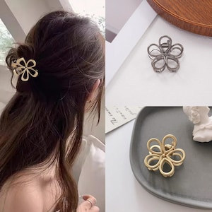 Peut inclure: Barrette en forme de fleur dorée dans les cheveux d'une femme. D'autres barrettes dans l'image incluent une barrette gris canon de fusil et une barrette dorée, toutes deux en forme de fleur. Les barrettes sont en métal.