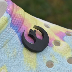 May include: A black Rebel Alliance symbol charm for a pair of tie-dye Crocs shoes.