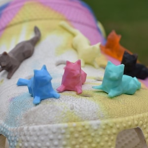 May include: A close-up of a pair of colorful clogs with a variety of small, colorful cat figurines on top. The clogs are white with a tie-dye pattern.