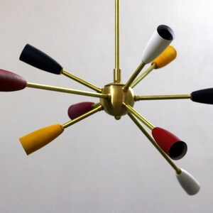 May include: A brass ceiling light fixture with eight arms, each with a different coloured cone-shaped shade. The shades are red, yellow, white, and black.