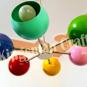 May include: A six-light ceiling fixture with colorful spherical shades. The shades are green, blue, red, yellow, and pink. The fixture has a chrome finish.