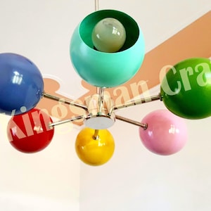 May include: A six-light chandelier with colorful globe-shaped shades in blue, red, green, pink, and yellow. The chandelier has a chrome finish and is suspended from the ceiling.