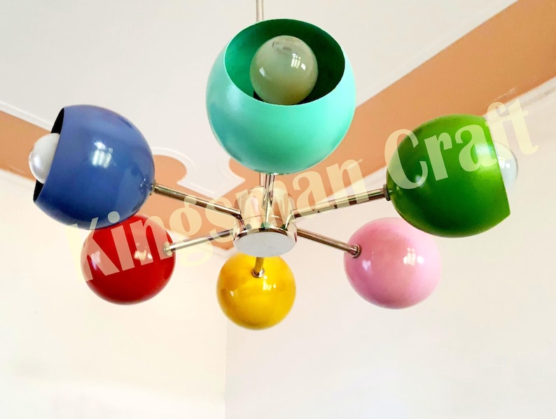 May include: A six-light chandelier with colorful globe-shaped shades in blue, red, green, pink, and yellow. The chandelier has a chrome finish and is suspended from the ceiling.