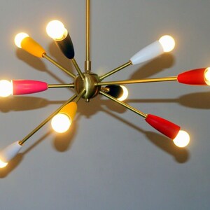 May include: A gold-toned, mid-century modern chandelier with eight light bulbs. The light bulbs are surrounded by coloured shades in red, yellow, pink, white, and black.