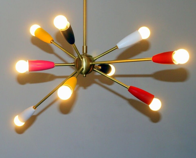 May include: A gold-toned, mid-century modern chandelier with eight light bulbs. The light bulbs are surrounded by coloured shades in red, yellow, pink, white, and black.