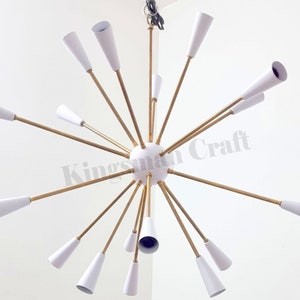 Puede incluir: Una lámpara de araña moderna blanca y dorada con 18 pantallas blancas en forma de cono. La lámpara de araña tiene un diseño de estrella con los brazos que se extienden desde una esfera central.