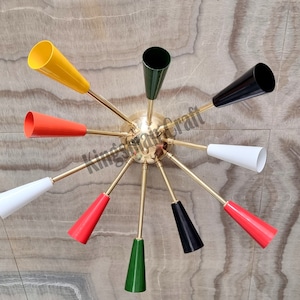 May include: A brass ceiling light fixture with eight arms, each ending in a cone-shaped shade. The shades are in various colours, including red, yellow, green, black, and white.
