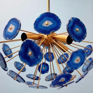 Puede incluir: Una lámpara de araña moderna con rodajas de ágata azul que irradian desde una esfera central dorada. Las rodajas de ágata son de un azul vibrante con detalles en blanco y dorado, creando una llamativa lámpara. La lámpara tiene múltiples brazos que se extienden hacia afuera.