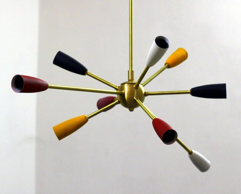 May include: A brass and multi-coloured mid-century modern chandelier with eight light bulbs. The chandelier has a starburst design with arms extending out from a central sphere. The light bulbs are covered in shades of red, yellow, white, and black.