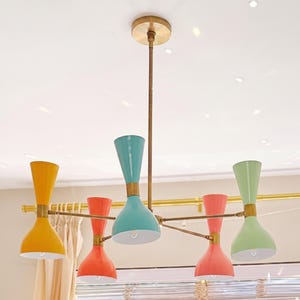 May include: A colourful chandelier with six lights. The light fixtures are in yellow, coral, teal, and green. The chandelier has a brass finish and is suspended from the ceiling.